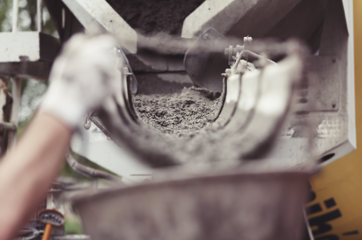 Wet concrete being poured from a mixer chute into a container.