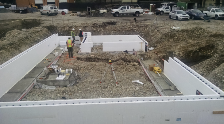 Construction site showing insulated concrete form walls set up for a foundation with workers and equipment inside.