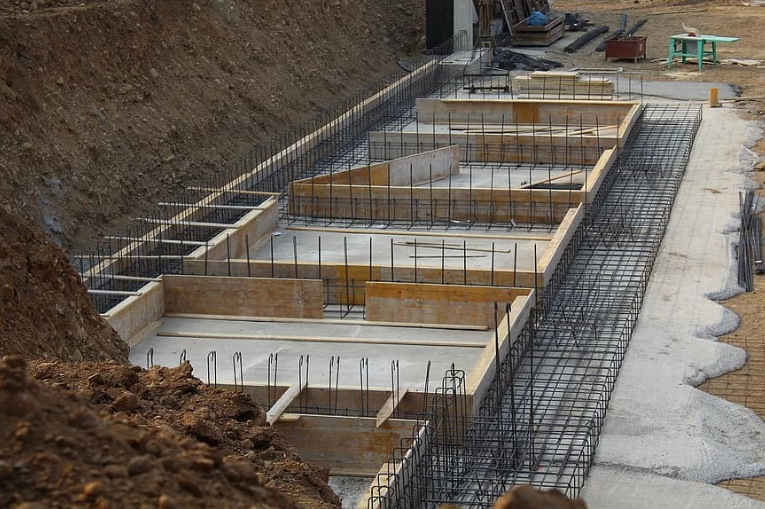 Reinforced concrete foundation under construction with footings, rebar, and foundation walls in place.