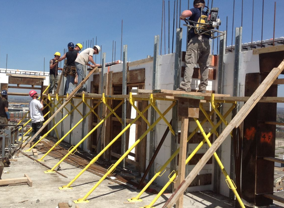 Construction crew working on elevated wall forms supported by yellow bracing on a multistory building site.