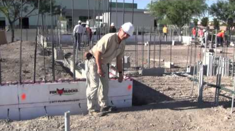 Worker installing a concrete stem wall with insulated forms and rebar at a construction site.