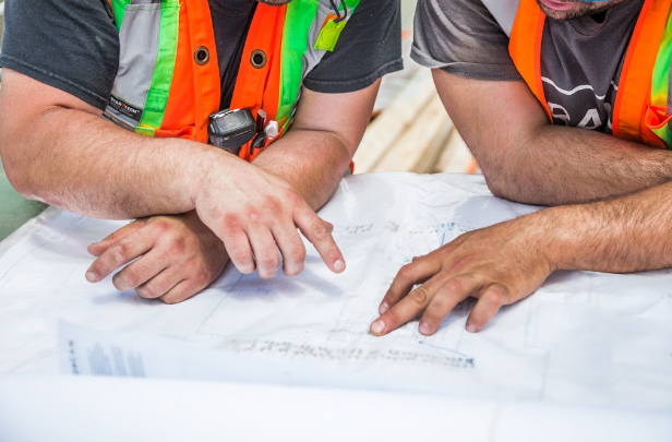 Alt Text: Two construction workers discuss the plans.