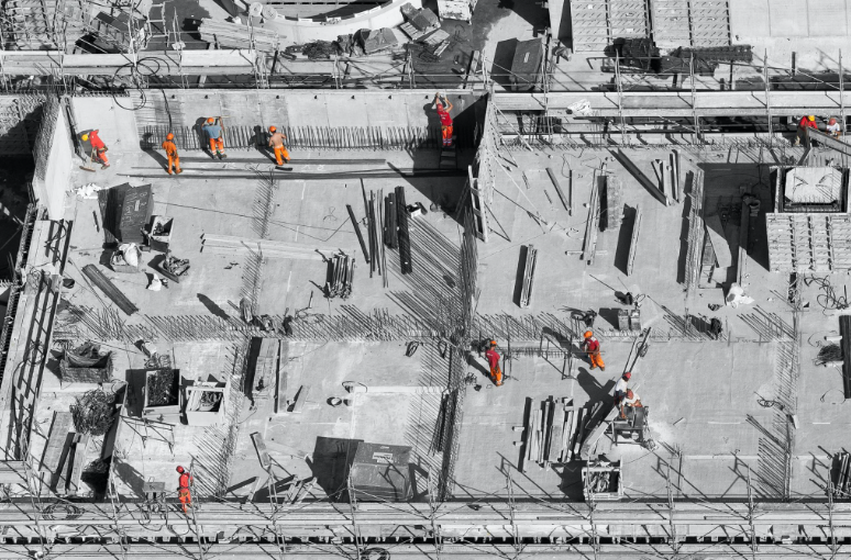 Aerial view of a commercial construction site with workers installing reinforced concrete and structural steel.